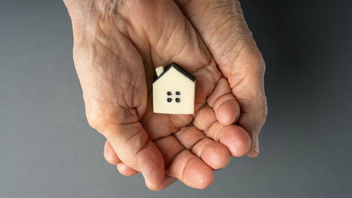 Elderly woman hands holds a little toy house. Inherited property idea.